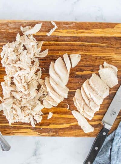 Boiled chicken shown on a cutting board with some shredded and some sliced.