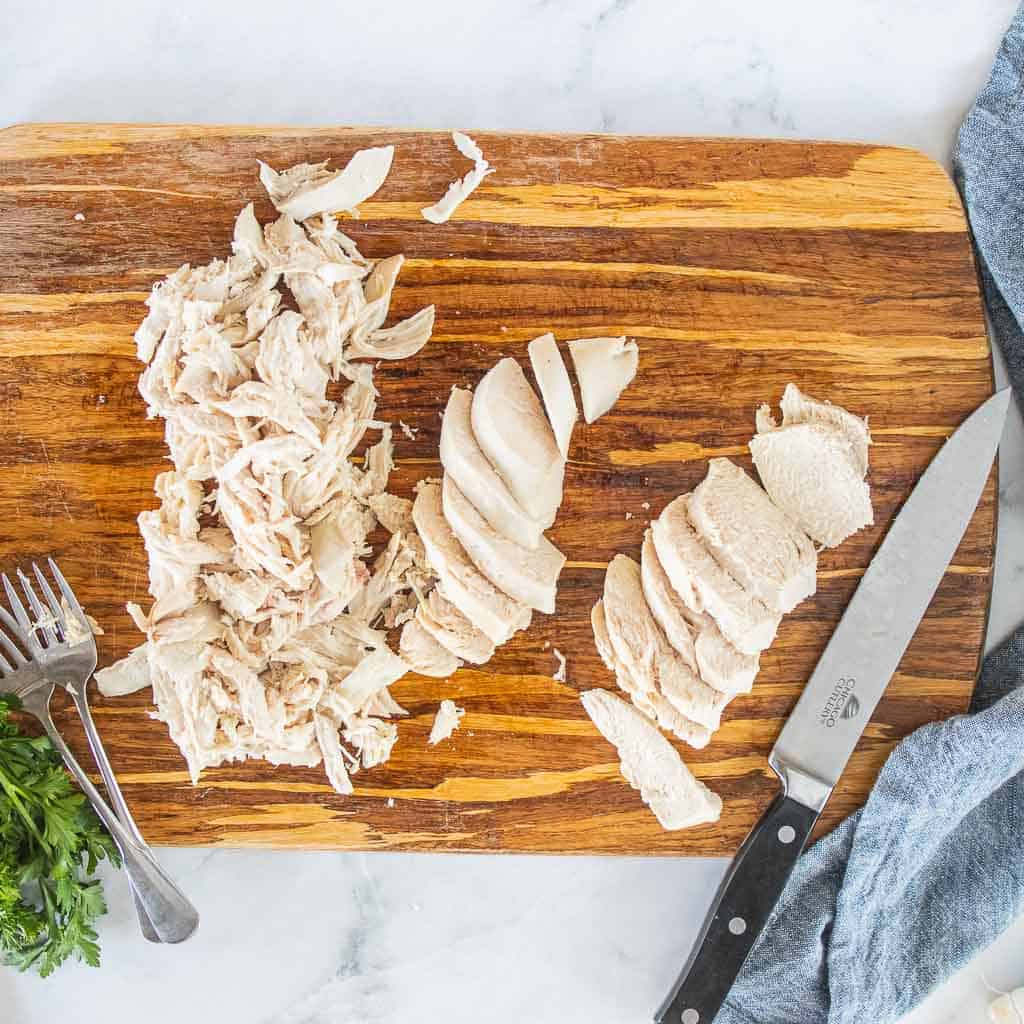 Boiled chicken shown on a cutting board with some shredded and some sliced.