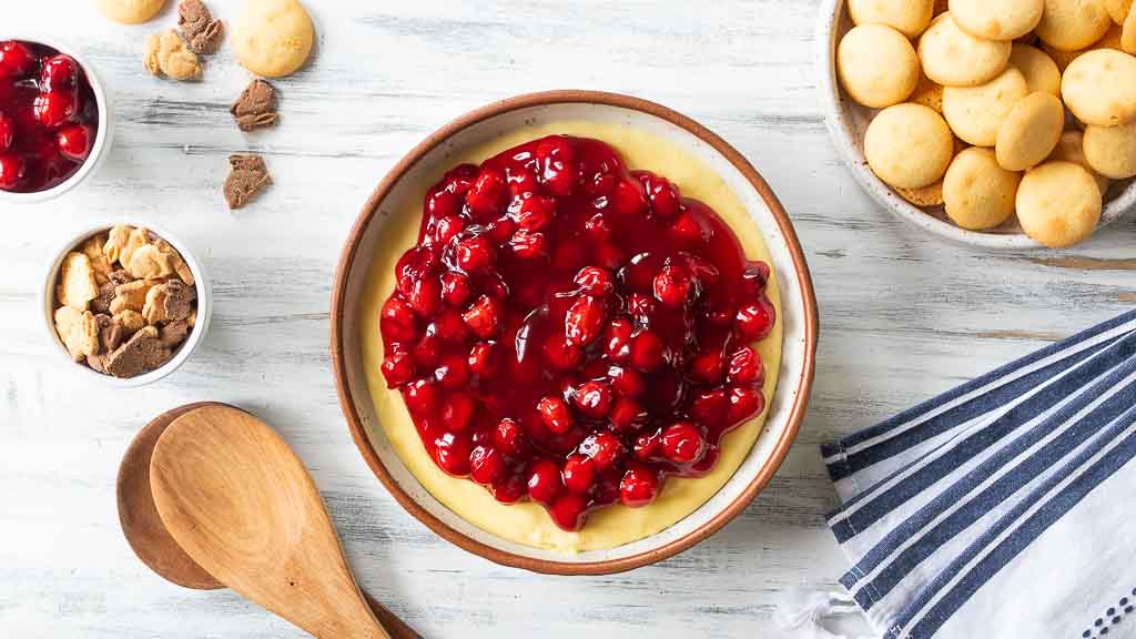 Cherry cheesecake dip in a bowl with gluten free vanilla wafers and crackers around it.