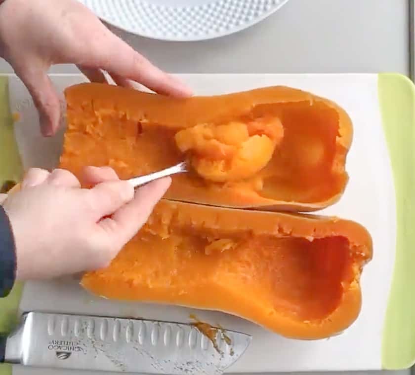 Two hands removing the flesh from a butternut squash that was cooked in a crockpot.