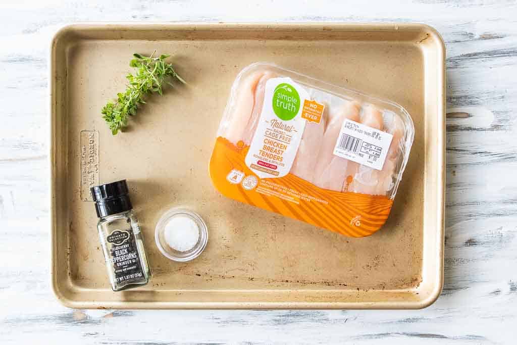 Top down shot of ingredients to boil chicken tenderloins including chicken, salt, pepper, and fresh herbs.