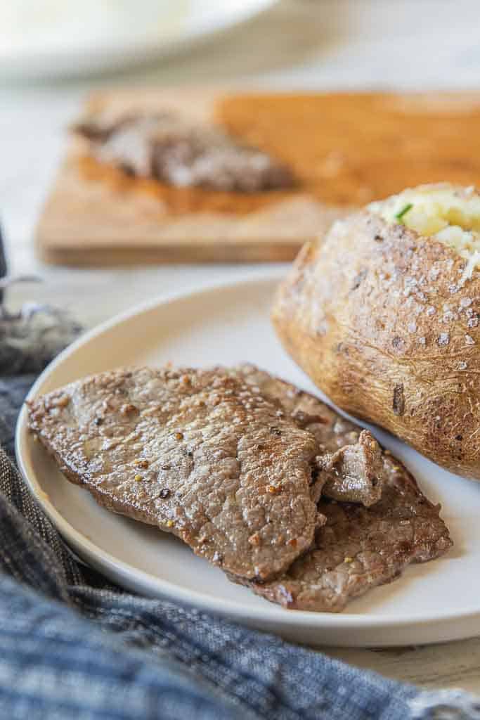 thin steak on plate with baked potato