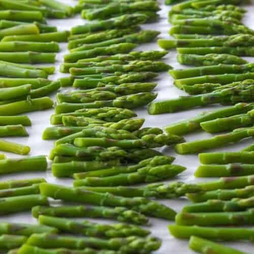 frozen asparagus stems on parchment lined baking sheet