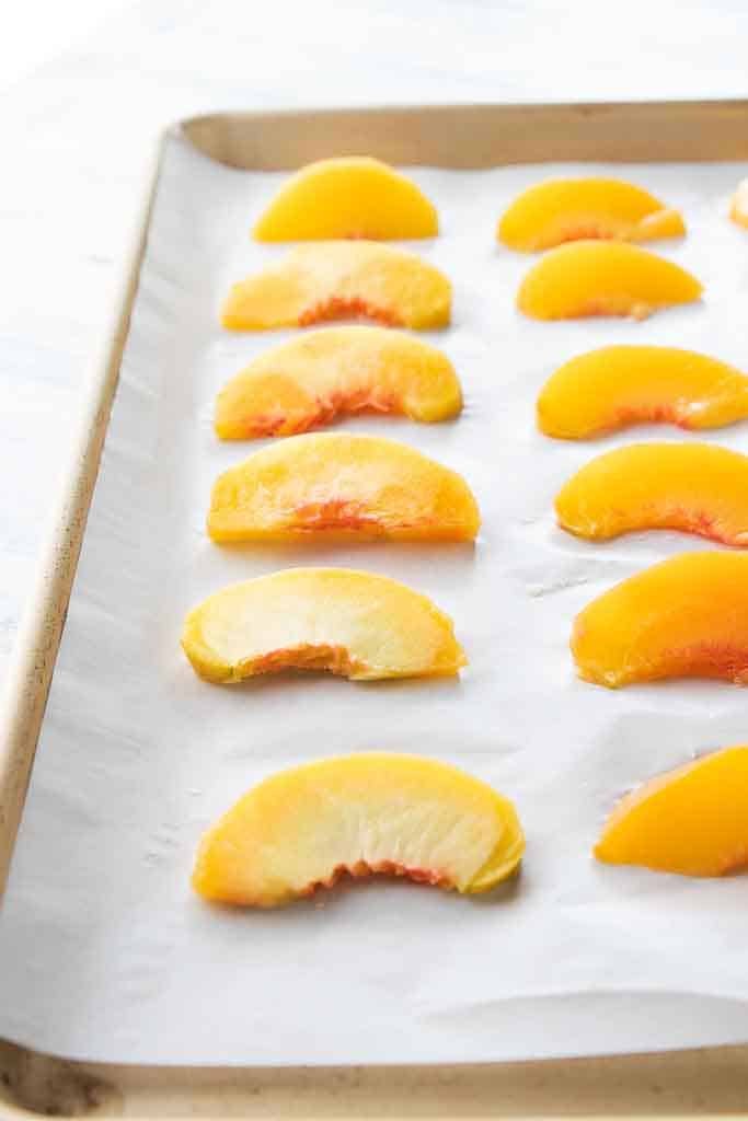 sliced peaches on parchment lined baking sheet
