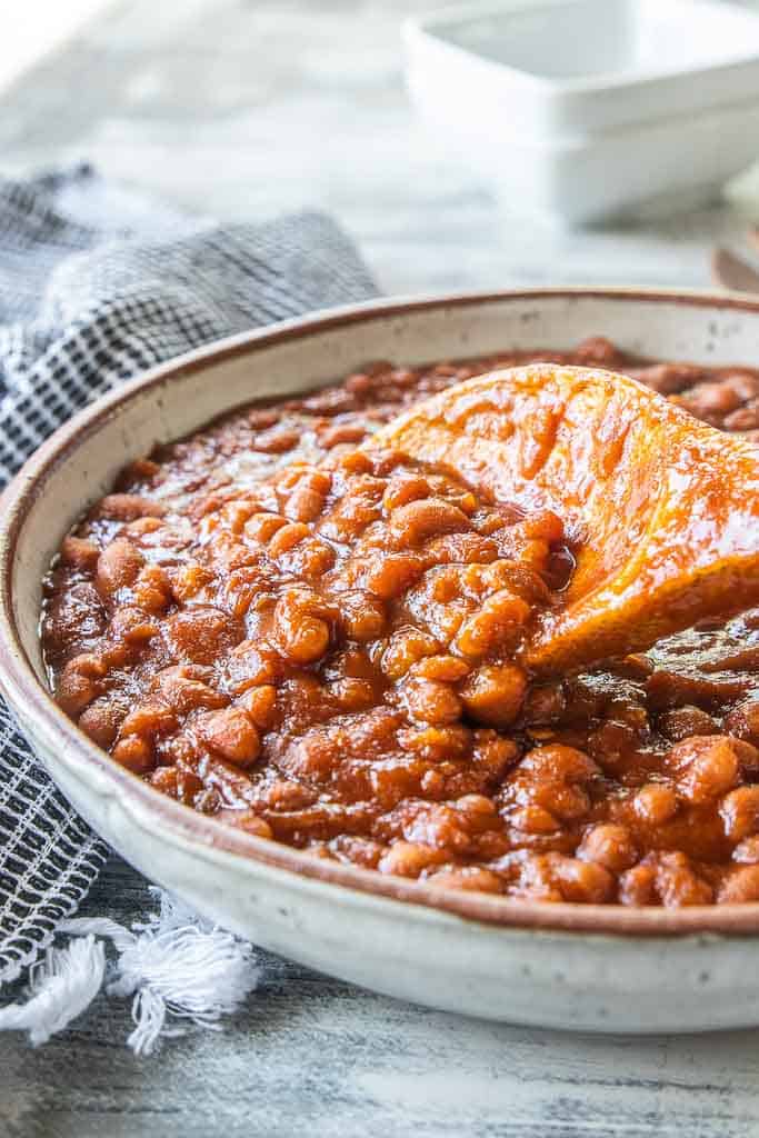 homemade baked beans in a serving bowl with wooden spoon