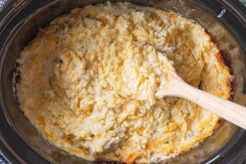 wooden spoon in crockpot filled with cheesy potatoes