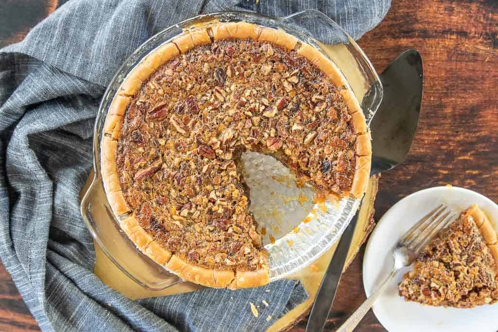 A top down view of a pecan pie with a slice removed on a plate next to the pie pan.