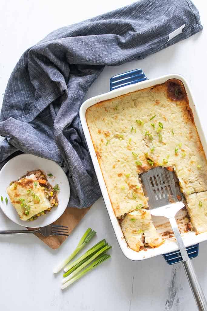 Top down pictures of a gluten free Shepards pie with a slice on a plate next to the casserole pan.