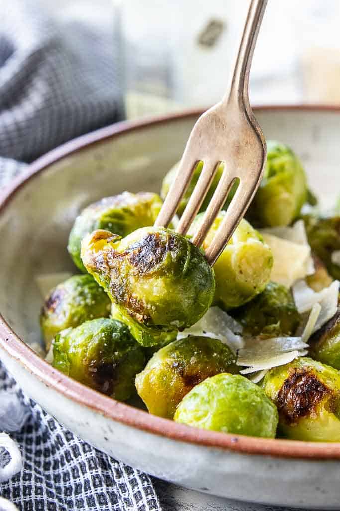 fork scooping brussels sprouts from a serving bowl