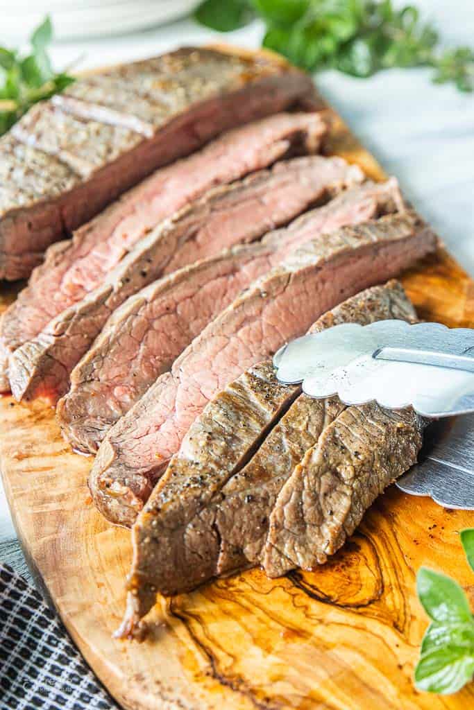 tongs picking up sliced flank steak