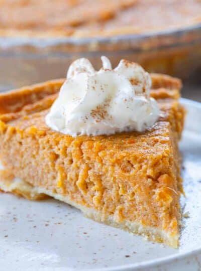 Sweet potato pie slice with whipped cream on a plate.