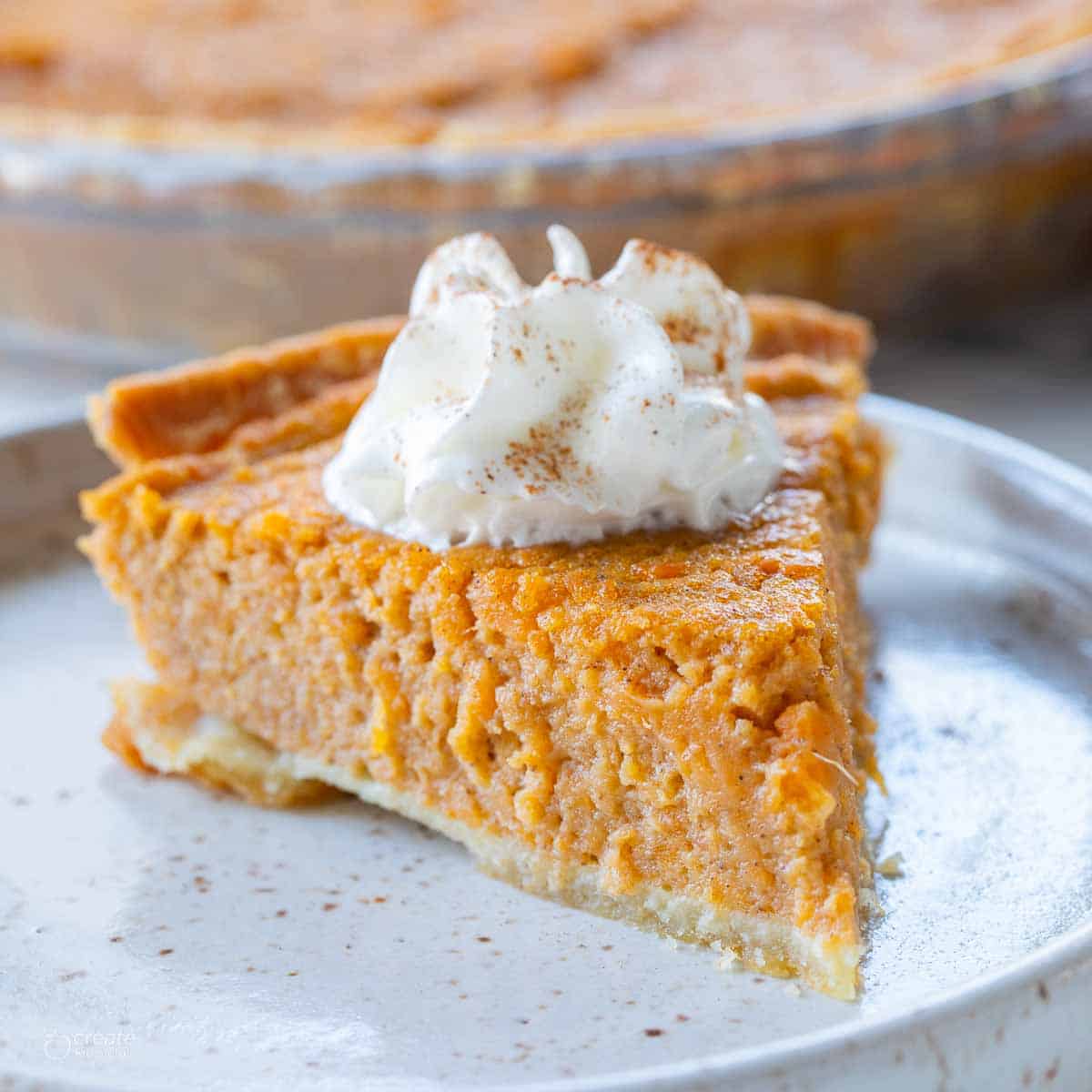 Sweet potato pie slice with whipped cream on a plate.