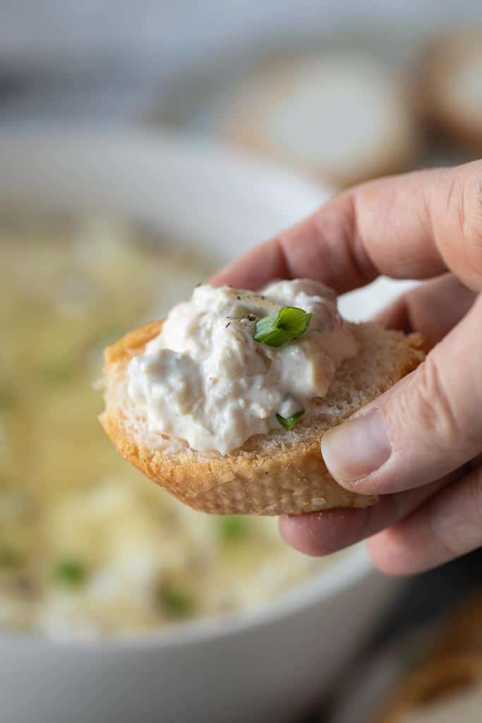 handing holding crostini topped with crab artichoke dip