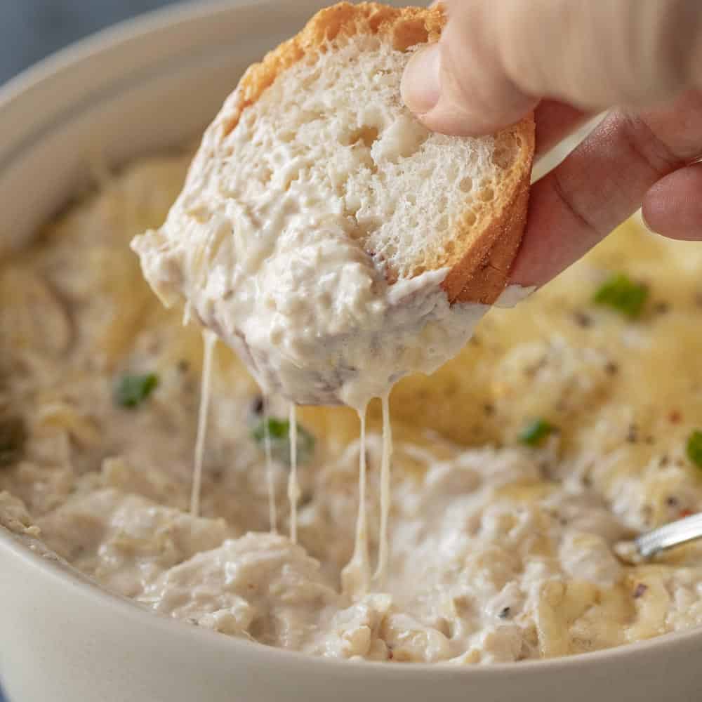 Crab artichoke dip showing a gluten free bread wedge scooping a cheesy bite.