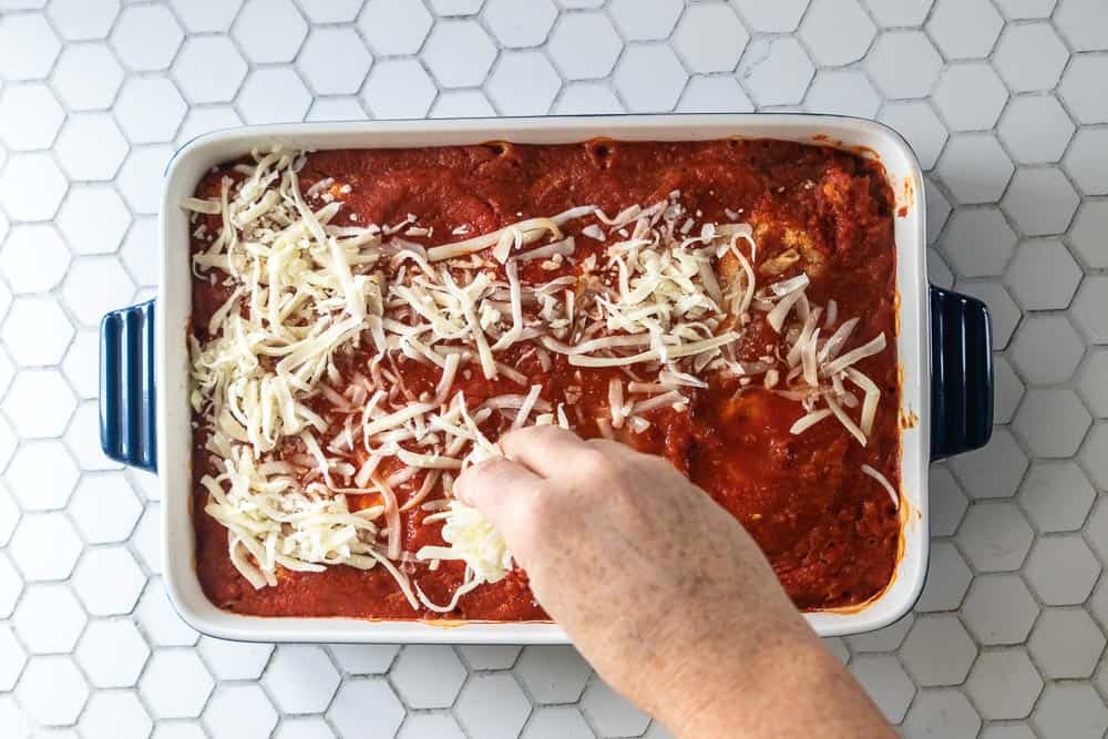 hand sprinkling mozzarella cheese on pasta bake