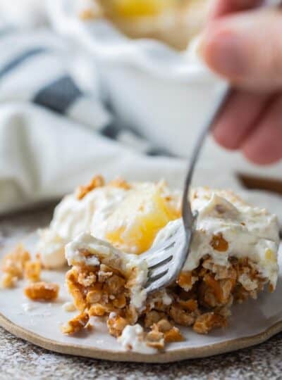 A close up of pineapple pretzel salad on a plate with a fork taking some.