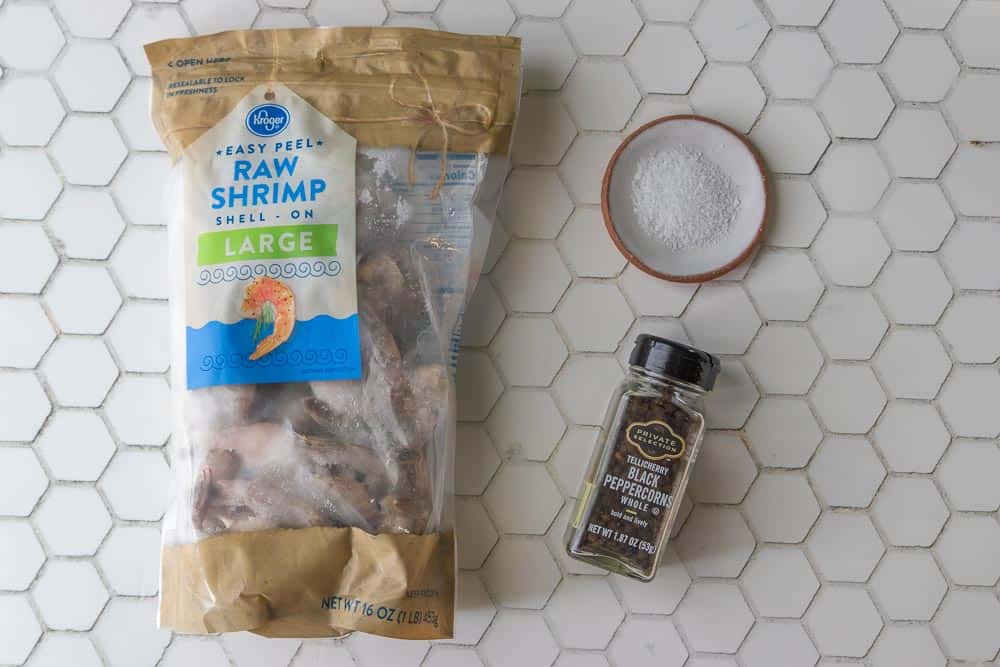 Ingredients to make poached shrimp including a bag of frozen shrimp, salt, and peppercorns.