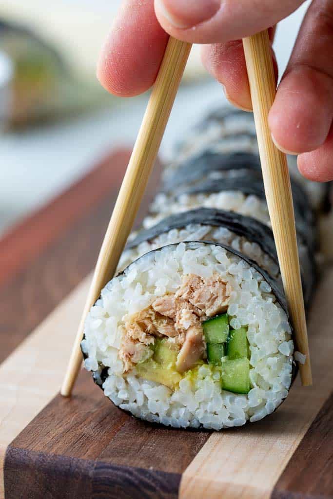 chopsticks picking up tuna sushi roll