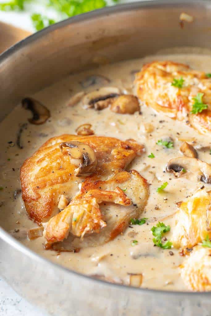 A close up of seared chicken in a skillet with mushroom sauce.