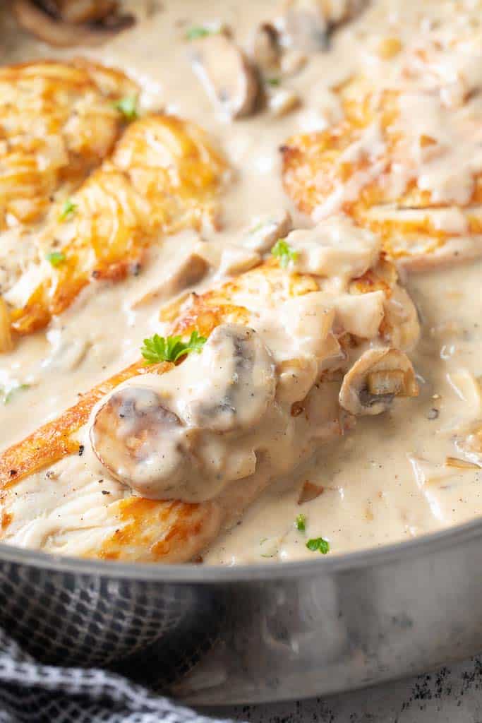 A close up of seared chicken in a skillet with mushroom sauce on top.