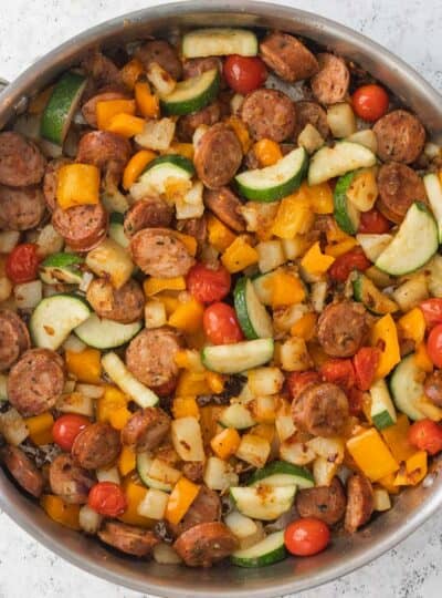top down shot of sauteed vegetables, potatoes and sliced sausage in skillet