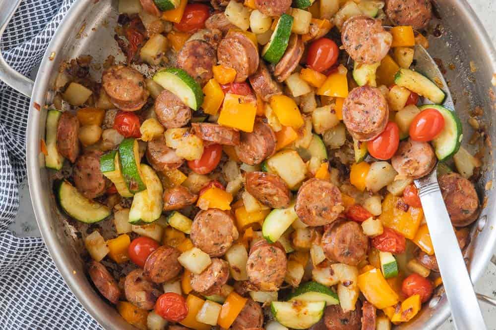 top down shot of sauteed vegetables, potatoes and sliced sausage in skillet