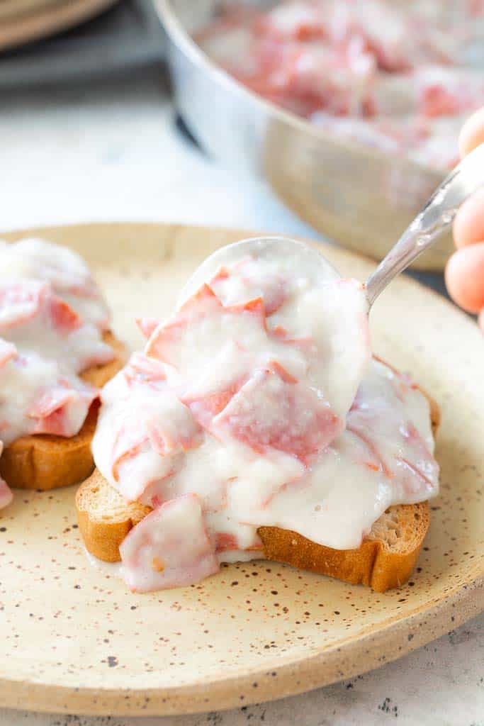 spoon placing chipped beef on a slice of toast