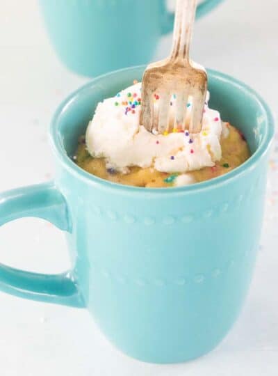 A fork taking a forkful of gluten free mug cake from a blue mug.