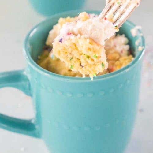 A fork taking a forkful of cake from a blue mug.