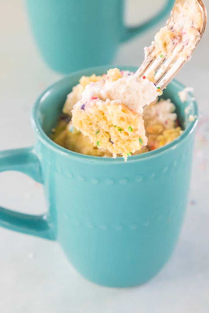 A fork taking a forkful of cake from a blue mug.