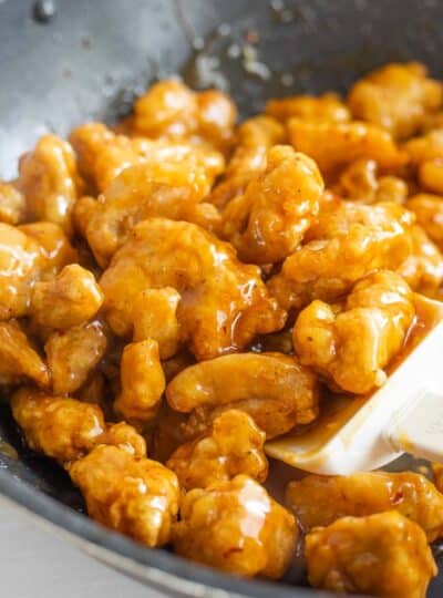 Gluten free orange chicken shown in a skillet with a spatula stirring.