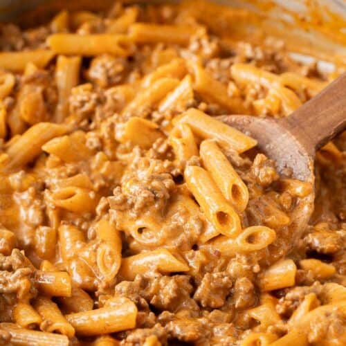 spoon stirring creamy pasta with ground beef in skillet