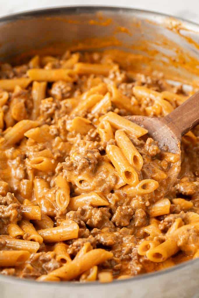 spoon stirring creamy pasta with ground beef in skillet