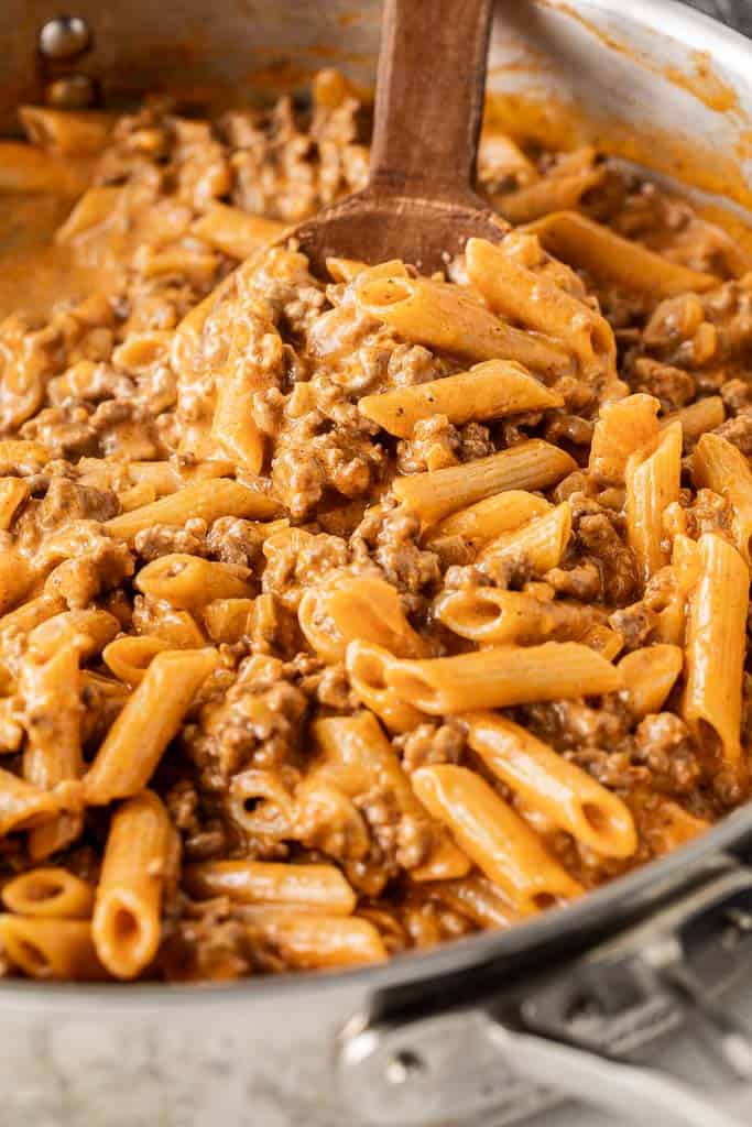 wooden spoon stirring skillet of creamy noodles with beef