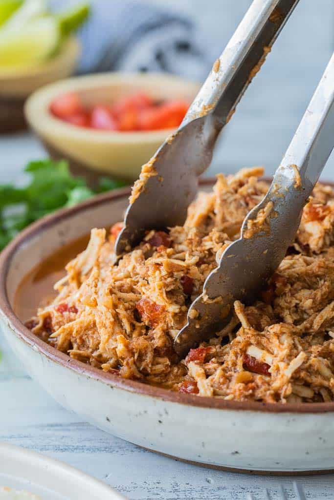 tongs scooping shredded chicken