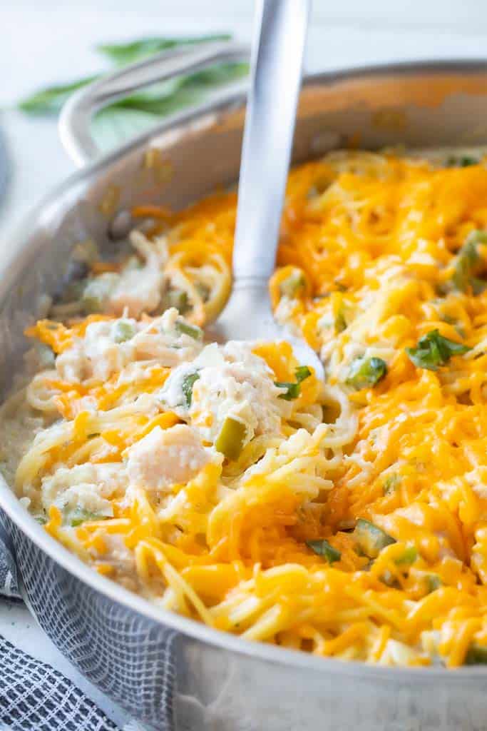 large spoon in skillet of cheesy chicken pasta