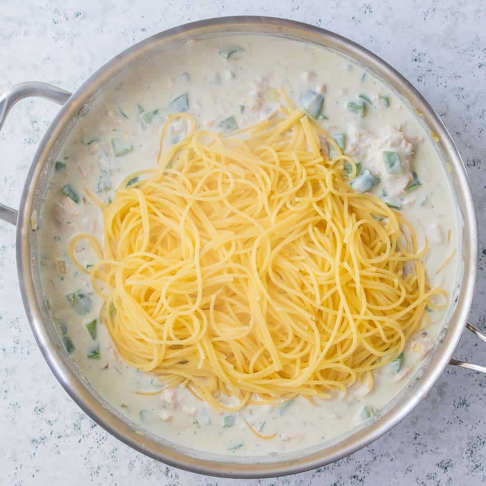 gluten free spaghetti added to creamy sauce in pan