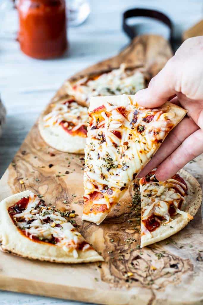 a hand holding up a piece of naan pizza