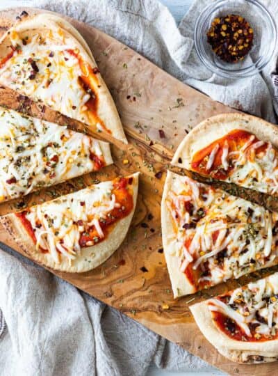 two naan pizzas sliced on a pizza board shown top down cropped square