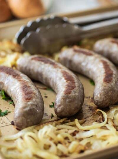 brats on a baking sheet with cooked onions