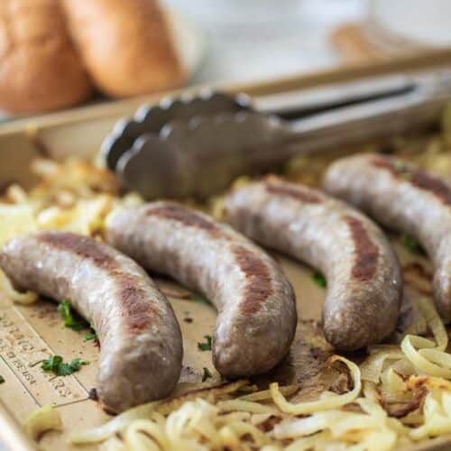 four baked brats on sheet pan with sliced onions
