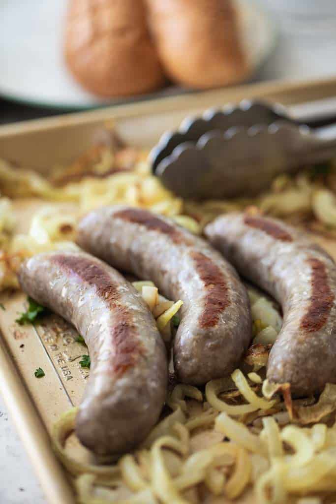 three brats on sheet pan with sliced onions