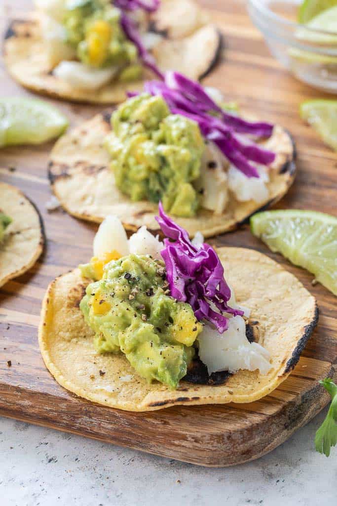 corn tortillas topped with fish, guacamole and cabbage