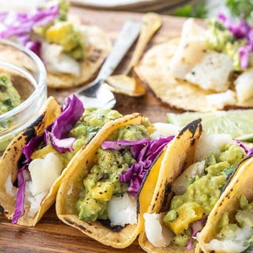 folded fish tacos topped with cabbage and guacamole