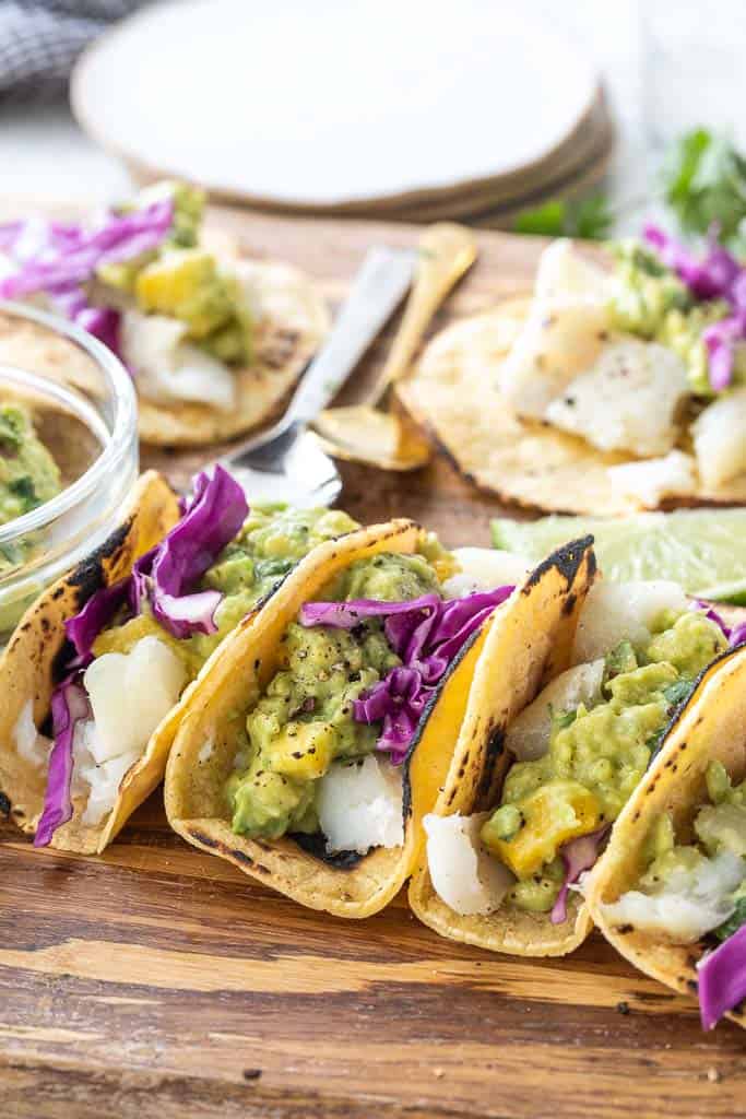 folded fish tacos topped with cabbage and guacamole