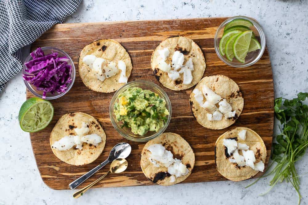 corn tortillas topped with cod surrounded by taco toppings