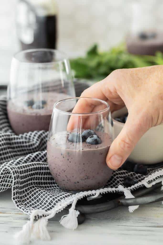 hand picking up glass filled with blueberry smoothie