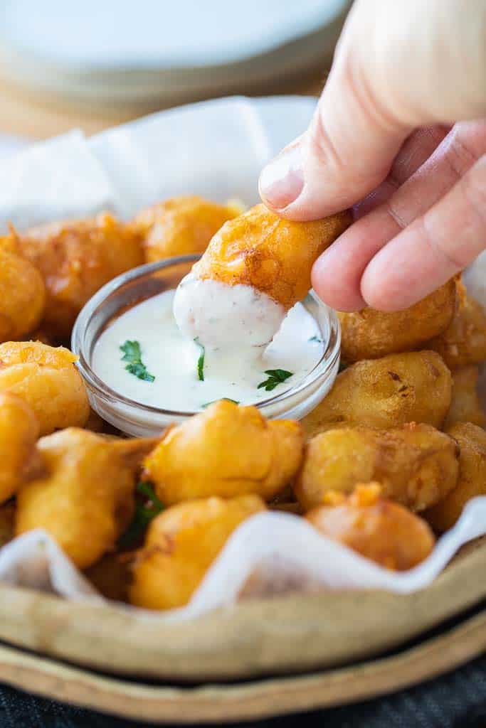 hand dipping cheese curd into dipping sauce.