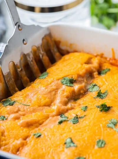 close up view of spatula in baking dish of enchiladas