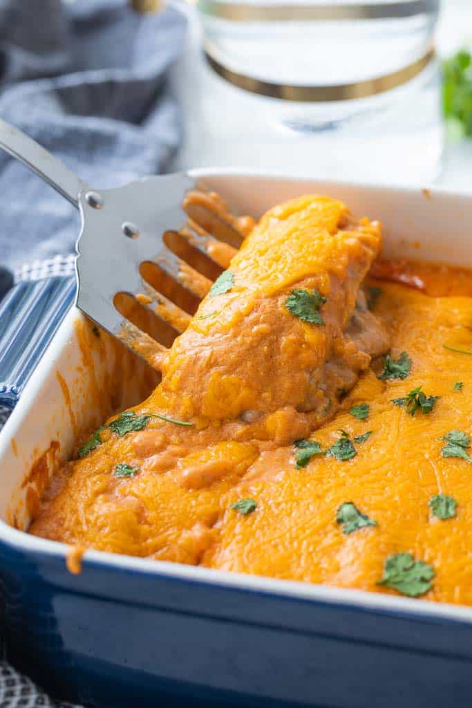 spatula scooping beef enchilada from a casserole dish